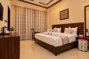 A hotel room with a large bed, a wooden headboard, a desk with a kettle, and a chair. - Vidhus Lado Home Ranthambhore (Sawai Madhopur)