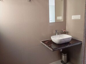 Ein Badezimmer mit Marmorplatte, einem weißen Waschbecken, einem Spiegel und einem an der Wand befestigten Lichtschalter.