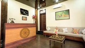 A reception area with a wooden reception desk, a sofa with colorful cushions, a framed picture on the wall, and a ceiling fan. - Vidhus Lado Home Ranthambhore (Sawai Madhopur)