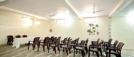 A conference room with a long table and chairs arranged in rows, ceiling fans, and windows with blinds.