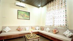 A living room with a beige sofa, colorful cushions, a wooden coffee table with a floral centerpiece, a framed painting on the wall, and a patterned curtain. - Vidhus Lado Home Ranthambhore (Sawai Madhopur)