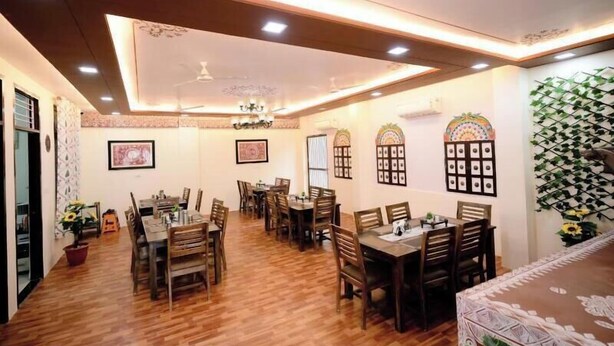 A dining area with wooden tables and chairs, ceiling lights, and framed artwork on the walls. - Vidhus Lado Home Ranthambhore (Sawai Madhopur)