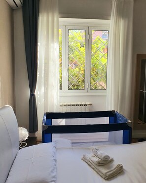 Une chambre d’hôtel avec un lit, une fenêtre avec des rideaux, un radiateur et une tête de lit bleue.