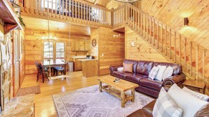 A spacious wooden cabin with a dining area, kitchen, and a living room with a leather sofa and a staircase. - Secluded Cherry Log Cabin w/ Hot Tub + Swings! (Cherry Log)