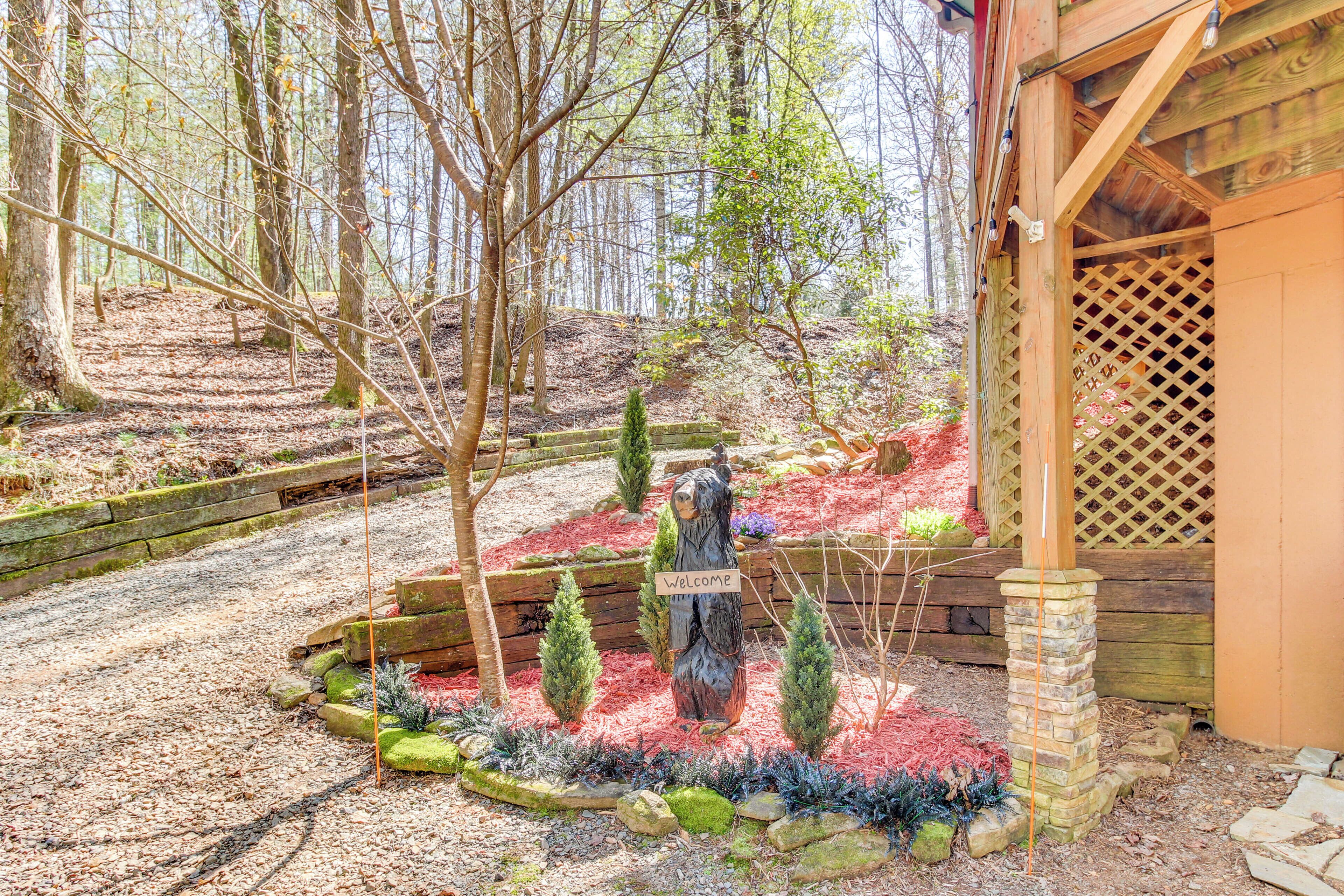 A wooden cabin with a lattice door, surrounded by a forested area with a 'Welcome' sign and decorative trees.