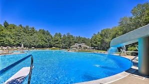 Una piscina con tobogán de agua, rodeada de árboles y tumbonas.