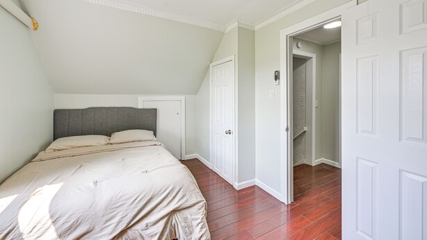 A bedroom with a bed, a wardrobe, and a door leading to a hallway.