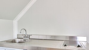 A kitchen with a stainless steel sink, a built-in range with two burners, and a white backsplash.