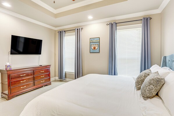 Un dormitorio con una cama grande, un aparador, un televisor de pantalla plana y una ventana con cortinas.