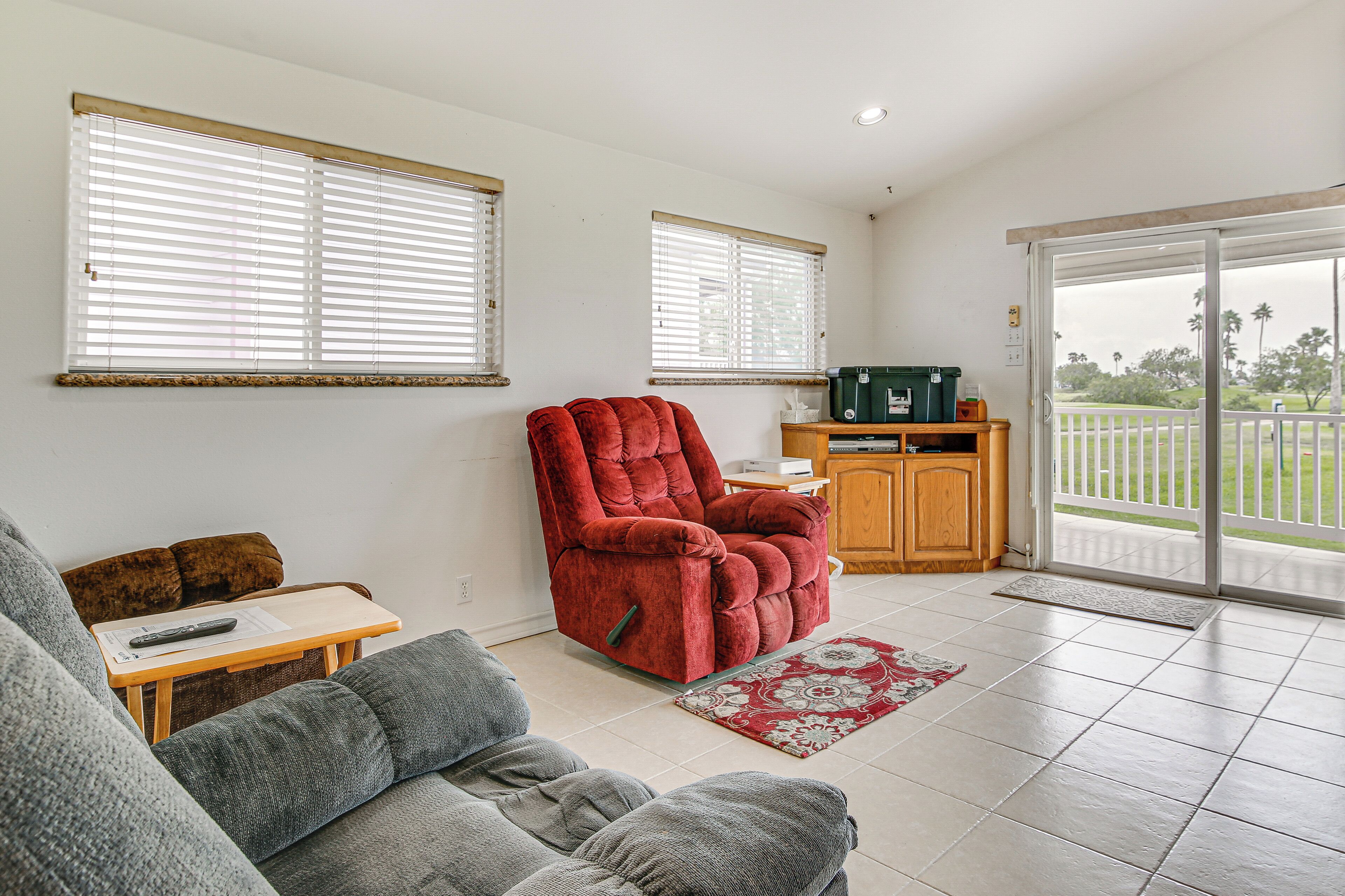 A living room with a grey sofa, a red recliner, a wooden table with a remote control, and a green storage box.