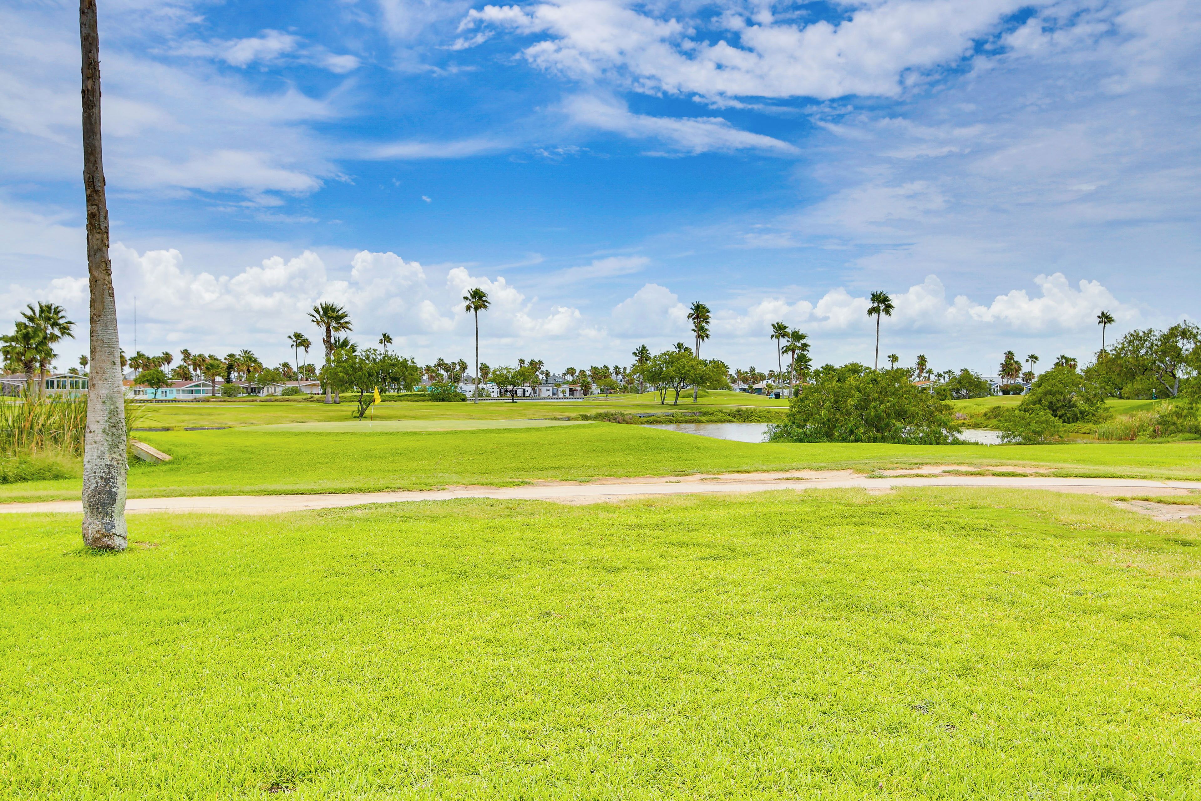 A golf course with a clear sky, palm trees, and a pond.