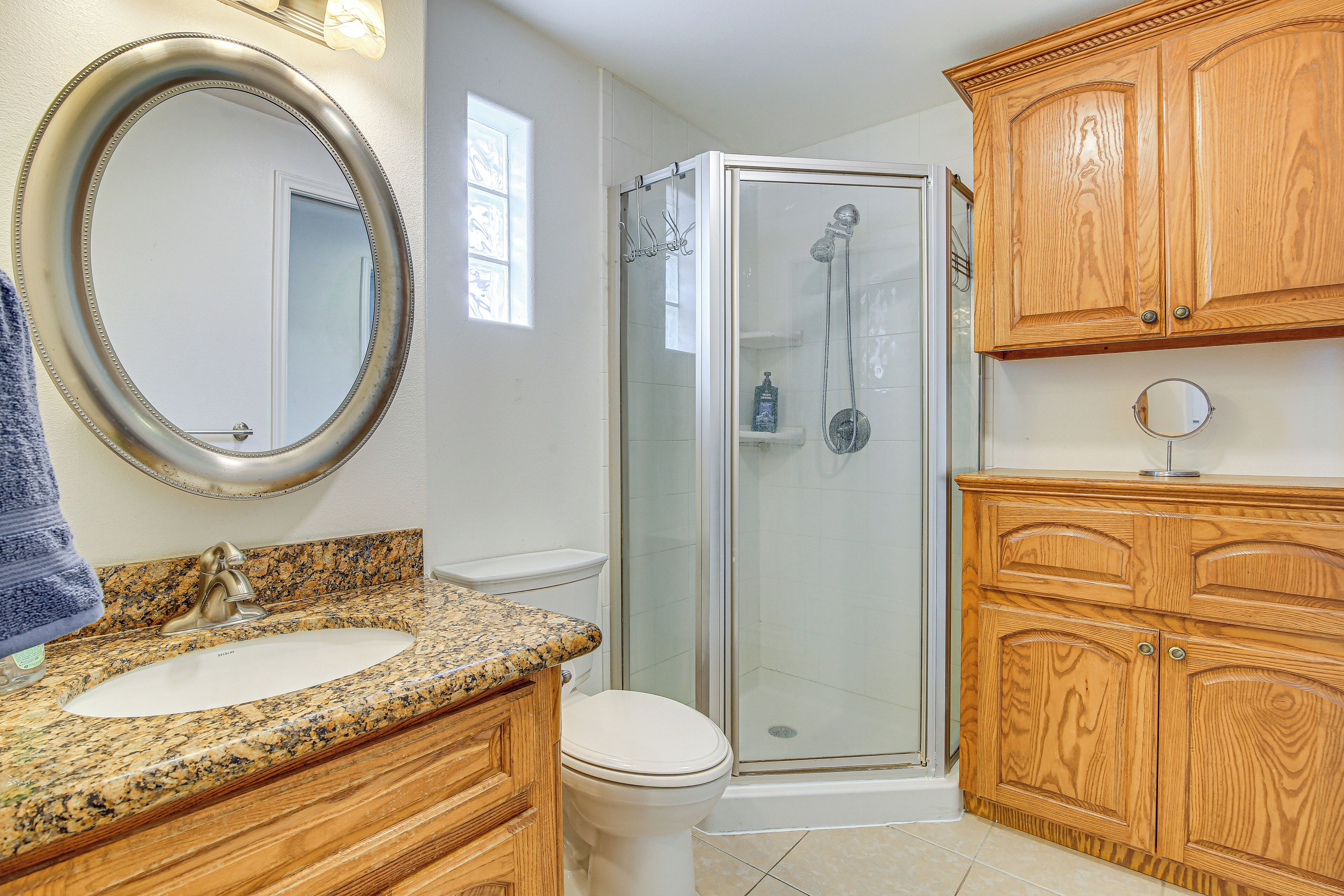 A bathroom with a granite countertop sink, a wooden vanity, a toilet, a glass-enclosed shower, and wooden cabinets.