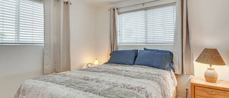 A bedroom with a bed, curtains, a bedside lamp, and a nightstand.
