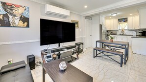 A modern living room with a flat-screen TV, a sofa, a coffee table, and a dining area with benches. - Pet-friendly Valley Stream Duplex - 1 Mi to Mall! (Valley Stream)