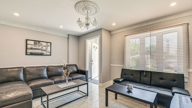 A living room with two black leather sofas, a coffee table, a chandelier, and a framed picture on the wall. - Pet-friendly Valley Stream Duplex - 1 Mi to Mall! (Valley Stream)