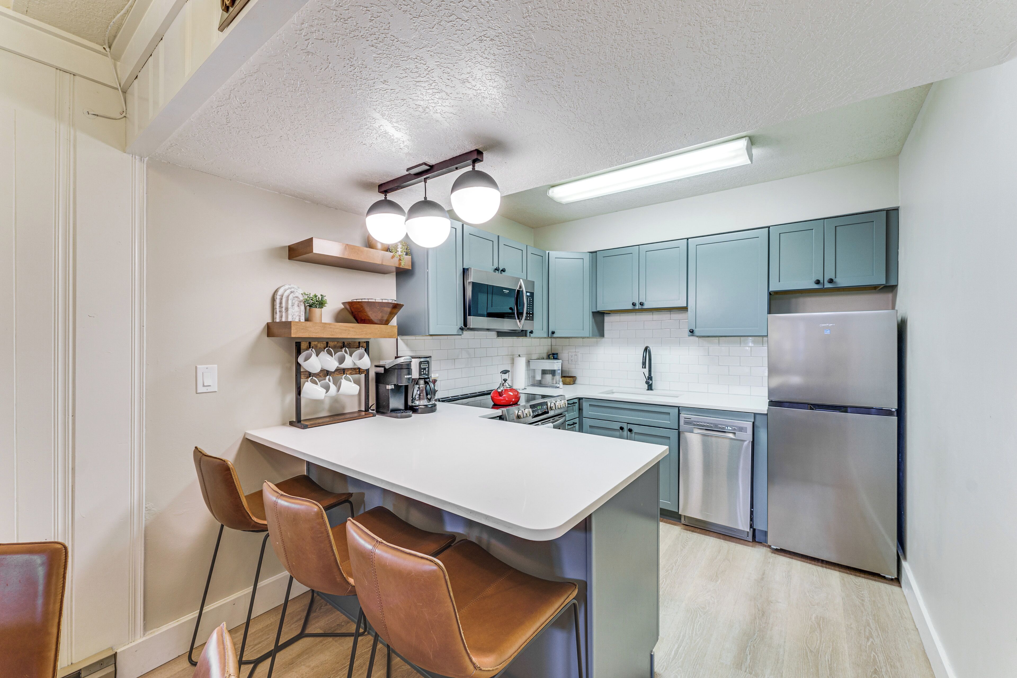 A modern kitchen with a central island, bar stools, a microwave, a refrigerator, and a dishwasher.