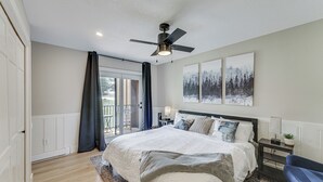 Ein Schlafzimmer mit einem großen Bett, einem Deckenventilator, einem Nachttisch, einem Sessel und Blick ins Freie durch eine Schiebetür.