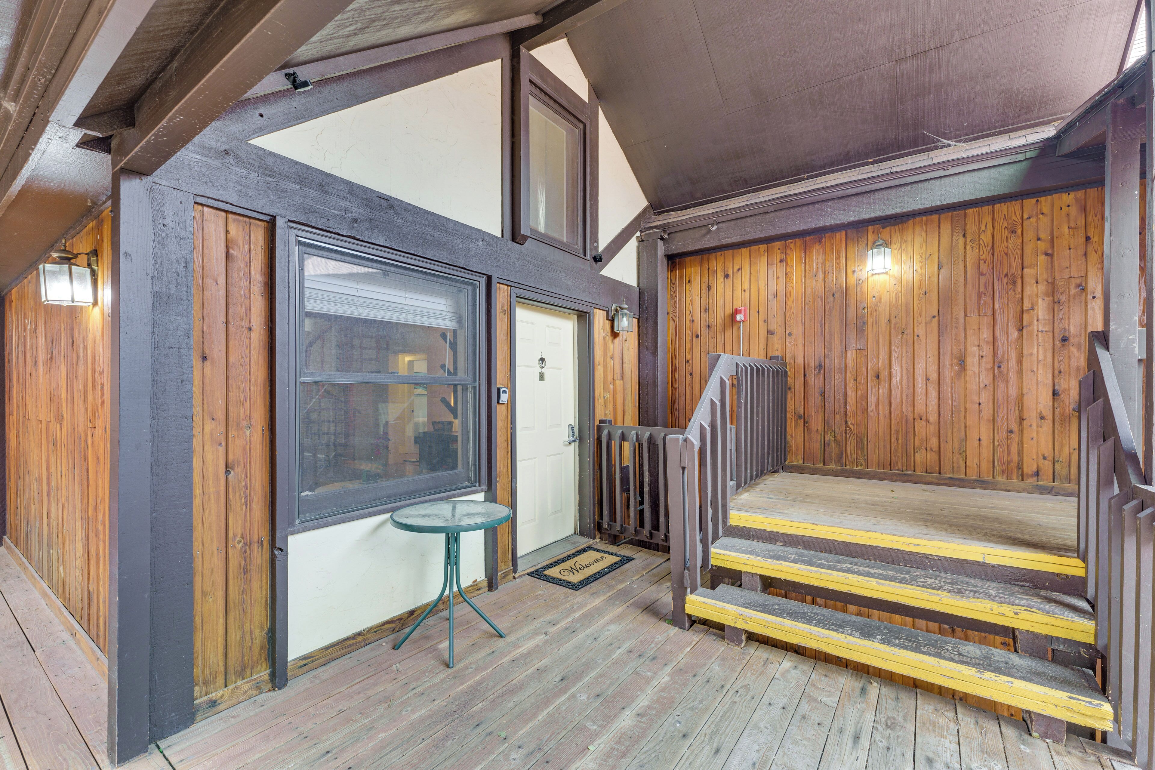 Fachada de madera con una puerta, una mesita y un conjunto de escaleras que conducen a un espacio cubierto.