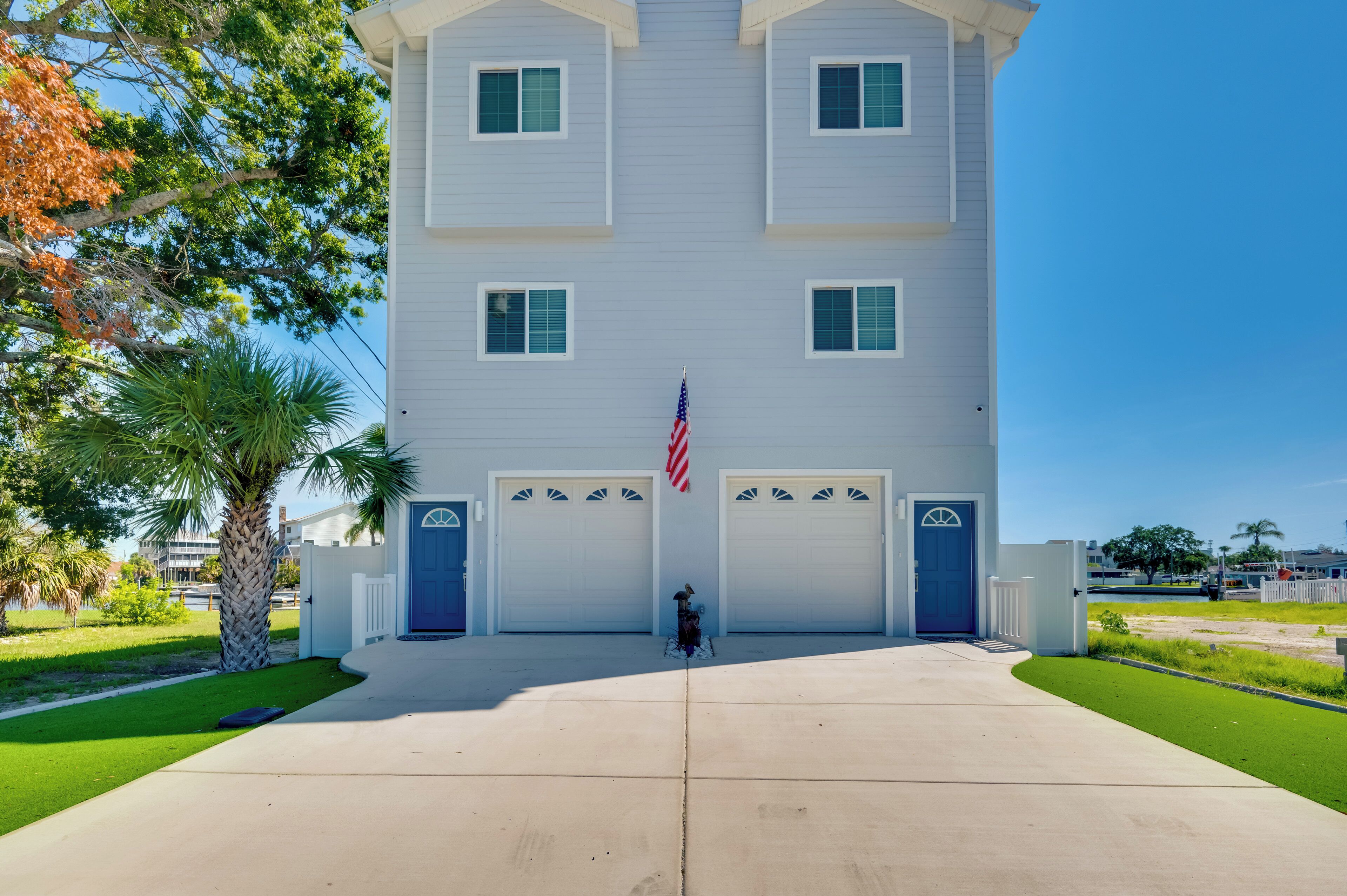 A two-story building with a symmetrical facade, featuring a central American flag, two garage doors, and a well-maintained lawn with a palm tree.