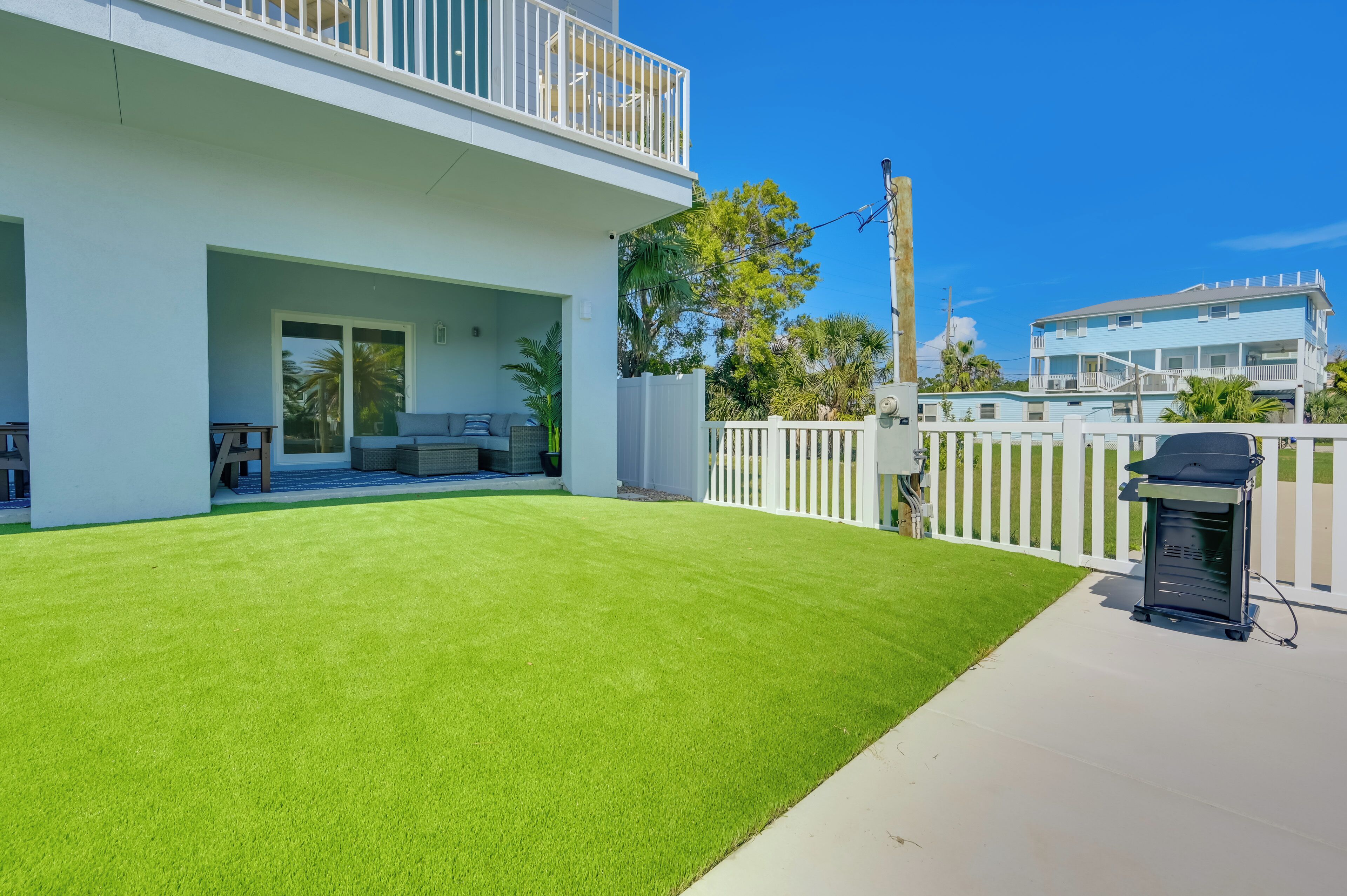 A modern two-story house with a well-maintained lawn, a patio with outdoor furniture, and a white fence.