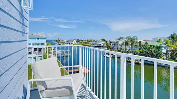 A balcony with a white railing overlooking a marina with boats and a clear blue sky.