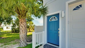 A house with a blue door, white railings, and a palm tree in the yard.