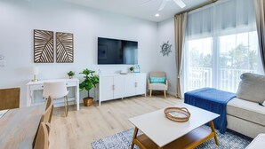 A modern living room with a white sofa, a dining table, and a TV mounted on the wall.