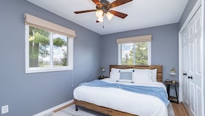 A bedroom with a bed, a ceiling fan, two windows with blinds, a nightstand, and a door. - Private 3BR Lakefront | Firepit + Kayaks | Near WI Dells (Oxford)