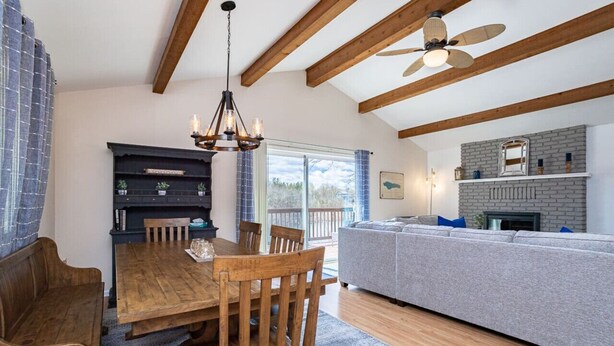 A spacious living area with a wooden dining table, a gray sofa, and a fireplace. - Private 3BR Lakefront | Firepit + Kayaks | Near WI Dells (Oxford)