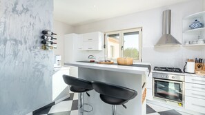 A modern kitchen with white cabinets, a central island with stools, a gas stove, and a built-in oven. - Villa Sv. Anna by Villas Guide (Radetici)