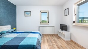 A bedroom with a bed, a TV on a stand, a window, and a radiator.