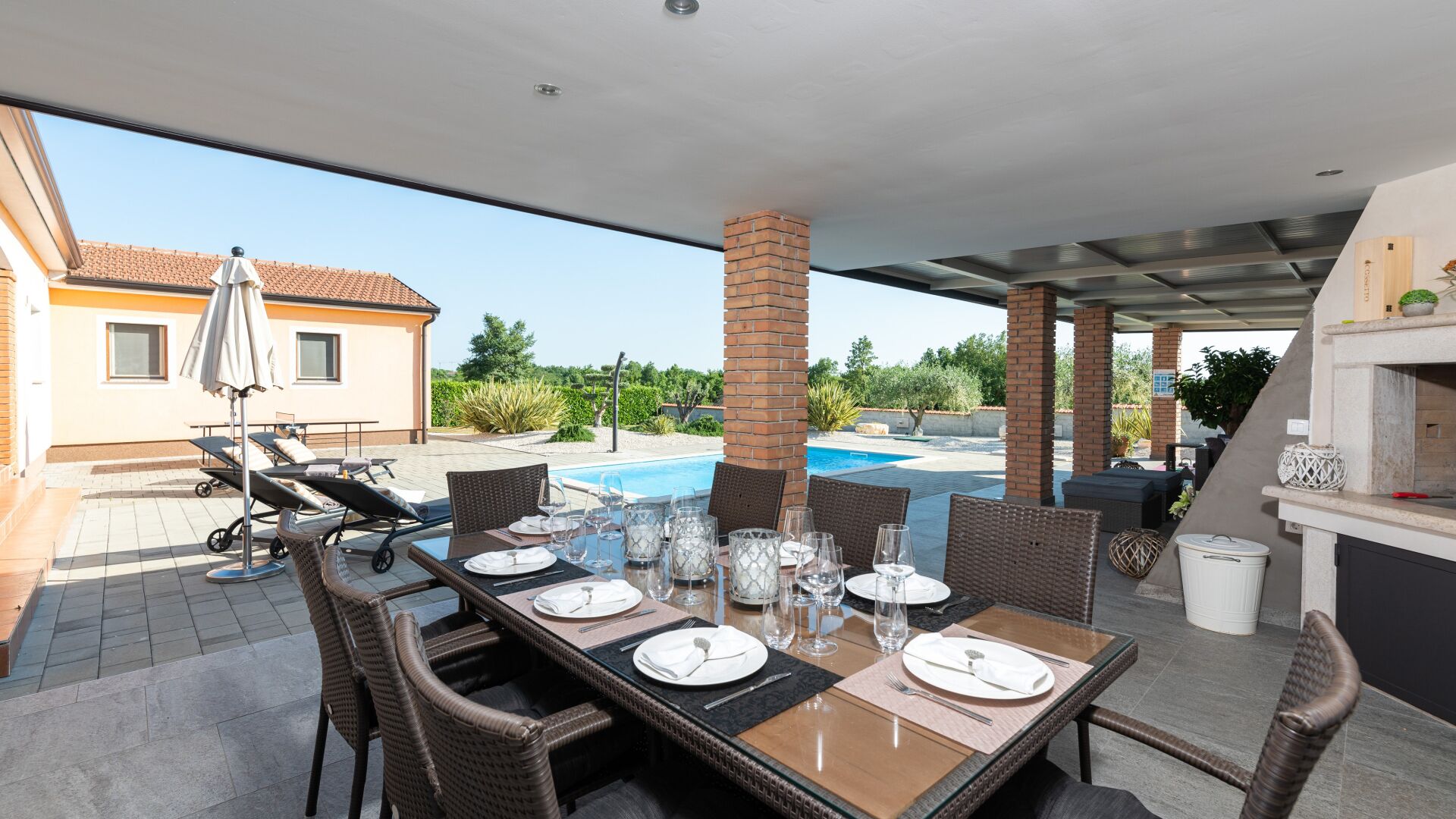 Un espace extérieur aménagé pour les repas, avec une piscine, des meubles en osier et un pilier en briques.