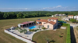 A large house with a swimming pool, a covered patio, and a well-maintained lawn.