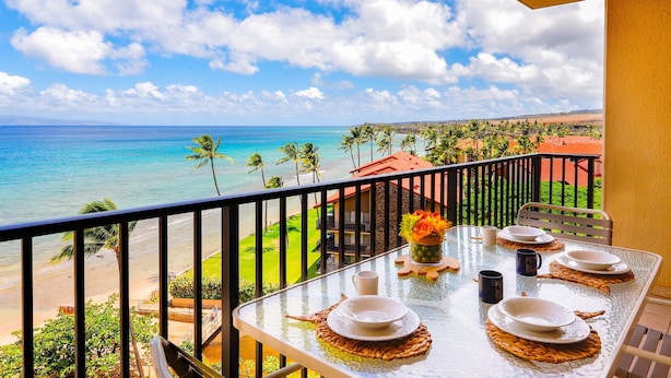 Un balcón con mesa lista para comer, con vista a una playa y el océano.