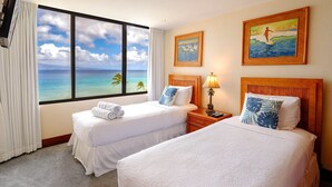 Una habitación de hotel con dos camas, vista al océano y decoración con motivos tropicales en las paredes.