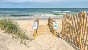 A wooden boardwalk leading to a beach with a 'KEEP OFF DUNES' sign and a 'NOTICE' sign indicating beach closure during certain hours. - 12BR Retreat w/ Private Pool, Theater, Volleyball + Elevator | Perfect for Large Groups (Corolla)