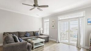 Uma sala de estar ampla com um sofá cinzento, uma mesa de centro de madeira e um ventilador de teto.
