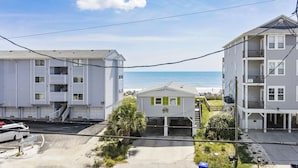 Uma área residencial à beira-mar, com edifícios altos, uma pequena casa de praia e vista clara para o oceano.