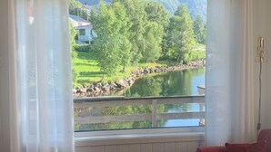 Quarto com uma grande janela com vista para um lago, dois sofás vermelhos, uma mesa de centro de madeira e um tapete estampado.