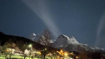 Una muntanya coberta de neu de nit, amb cases i fanals al primer pla.
