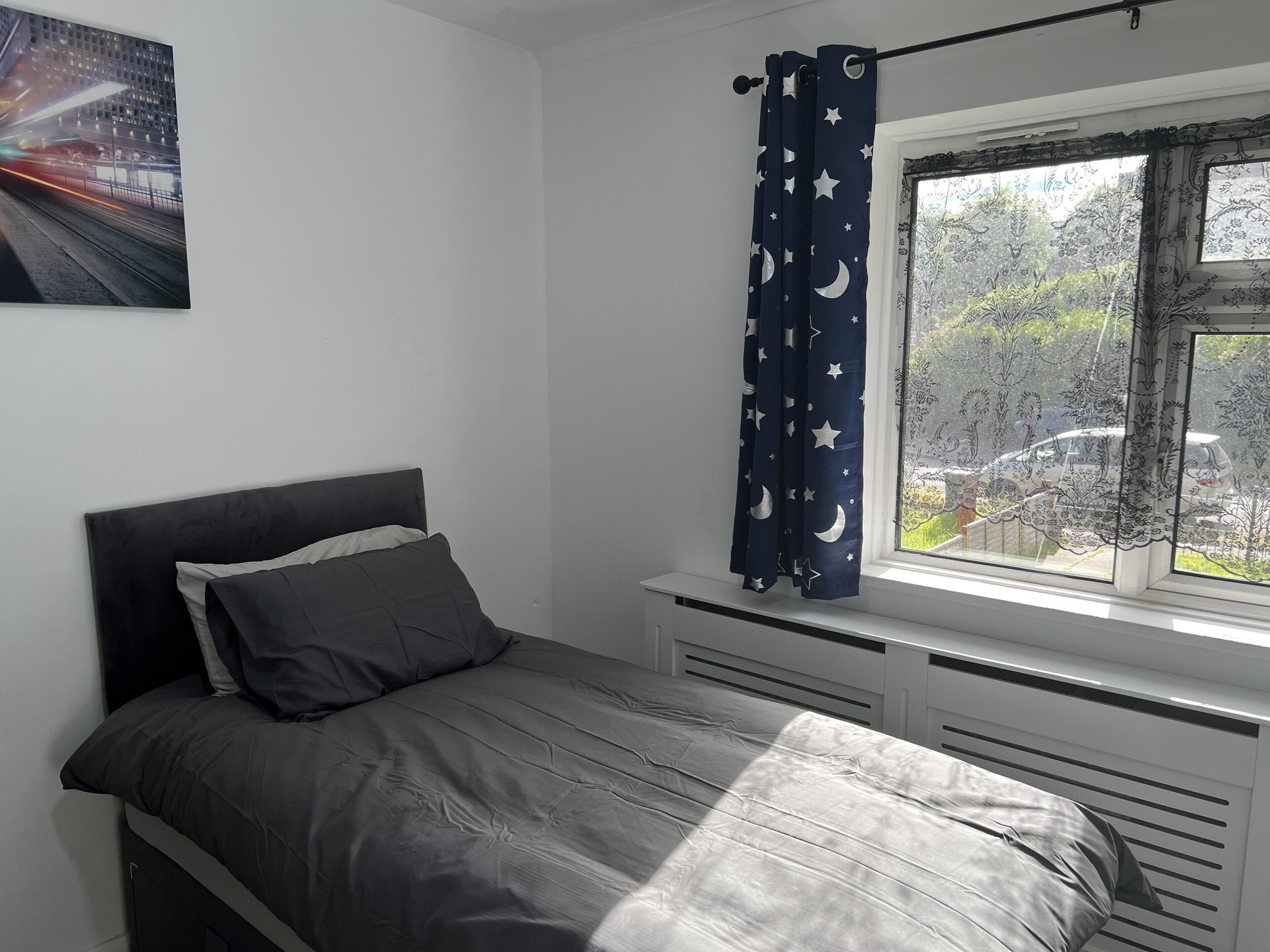 A bedroom with a bed, a window with a view of the outside, and a curtain with a star pattern.