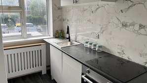 A modern kitchen with a black countertop, white cabinets, a window with a view of the street, and a built-in stove. - Comfy 2-bedroom Apartment (Birmingham)