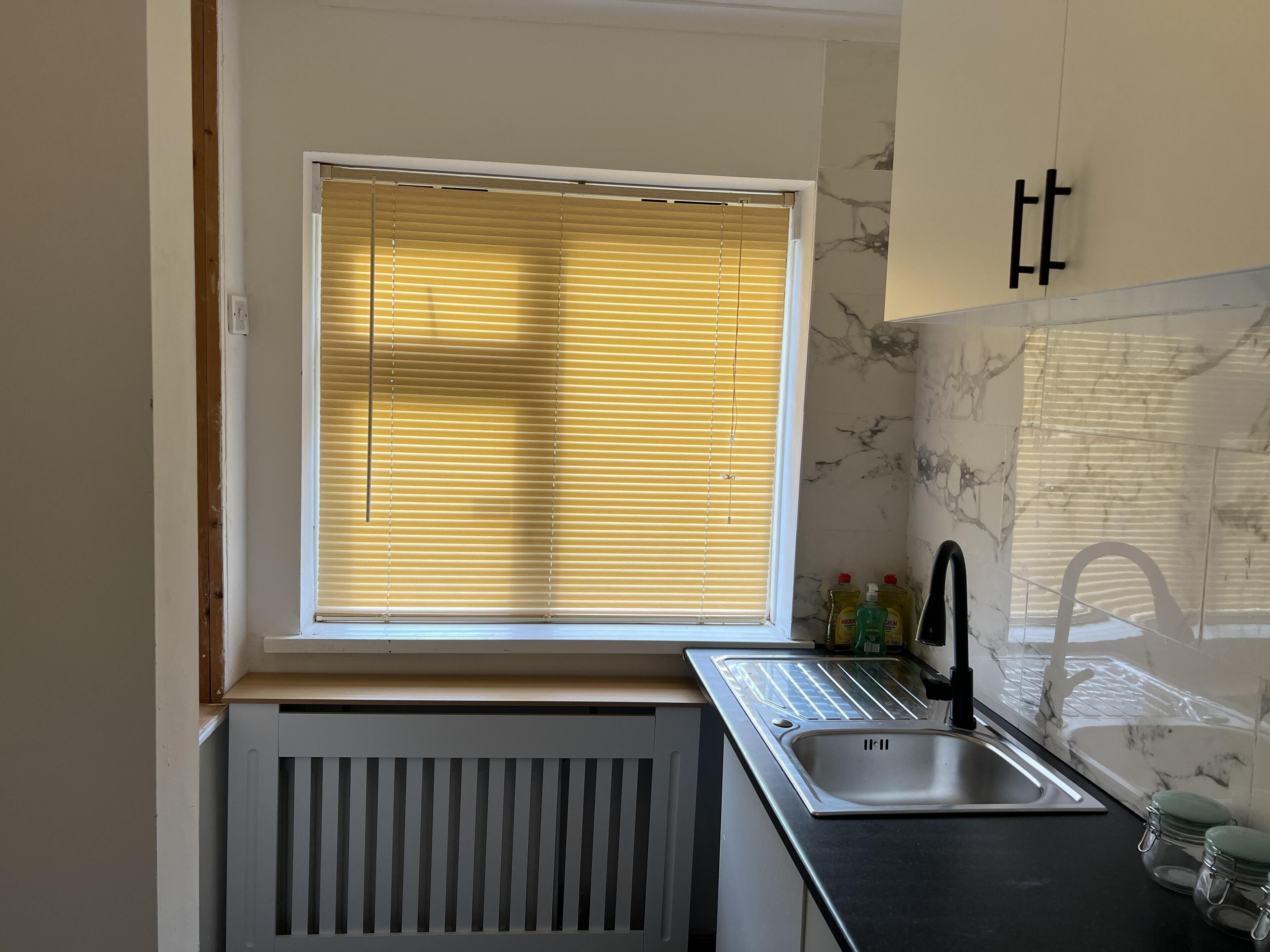 Eine kleine Küche mit Fenster, Spüle und Heizkörper.