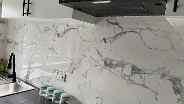 A kitchen with white marble tiles, a black range hood, a stainless steel sink, and four glass jars with teal lids. - Comfy 2-bedroom Apartment (Birmingham)