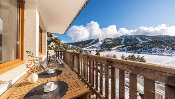 Eine Holzterrasse mit Sitzgelegenheiten und Blick auf schneebedeckte Berge.