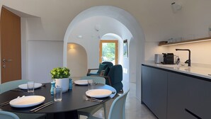 A modern kitchen with a dining area. There is a table set for two with plates, cutlery, and glasses. A potted plant is on the table. The kitchen has a countertop, sink, and a coffee machine. - A Trullo Like No Other - Timeless Style, Modern Comforts. Private Pool (Selva di Fasano)