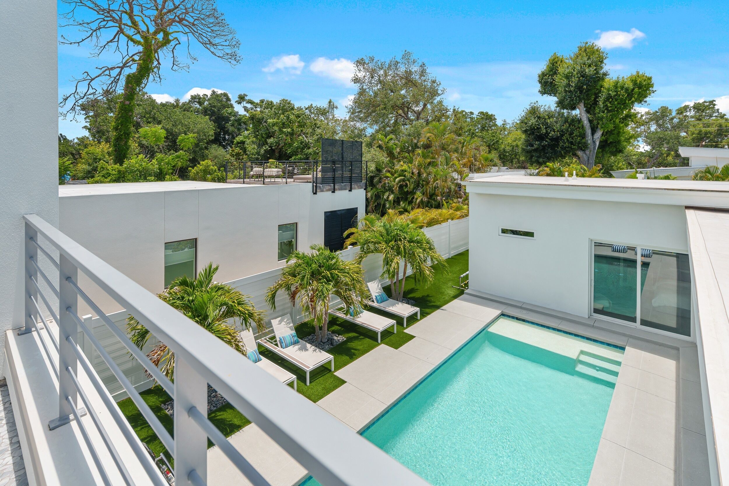 Un espace piscine extérieur moderne, doté de chaises longues, d’une piscine et d’un aménagement paysager luxuriant.