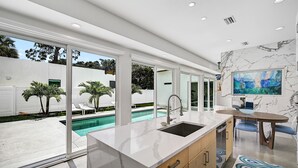 A modern kitchen with a large island, a built-in sink, and a view of a swimming pool. - Paradise Found 3 Bedroom Home by RedAwning (Sarasota)