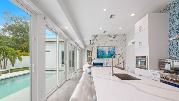 A modern kitchen with a marble backsplash, large windows, and a view of a swimming pool. - Paradise Found 3 Bedroom Home by RedAwning (Sarasota)