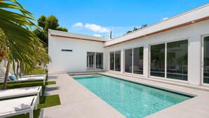 A modern pool area with a clear pool, white lounge chairs, and a white building with large windows. - Paradise Found 3 Bedroom Home by RedAwning (Sarasota)